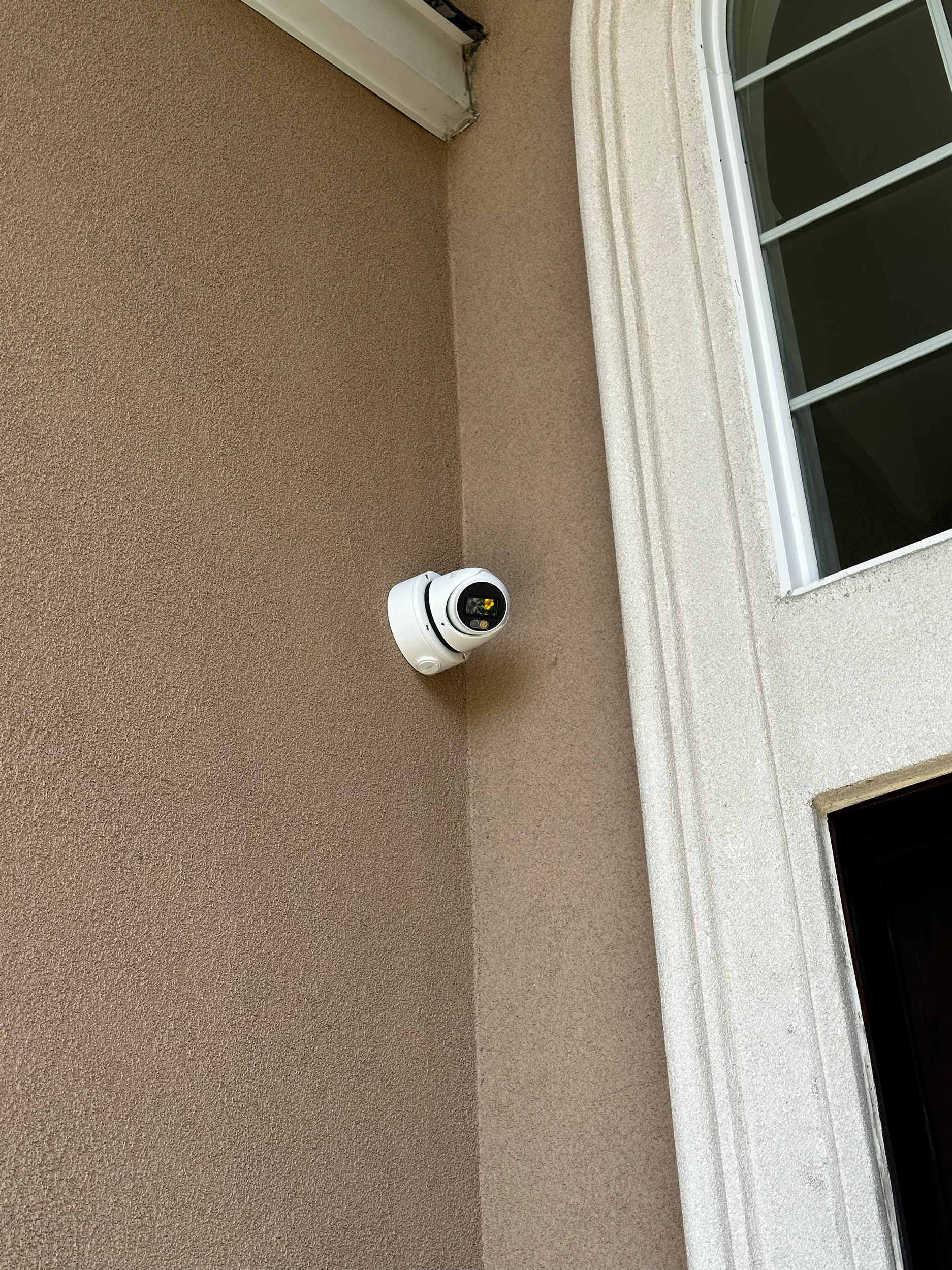 A security camera mounted on a beige stucco wall near a window.