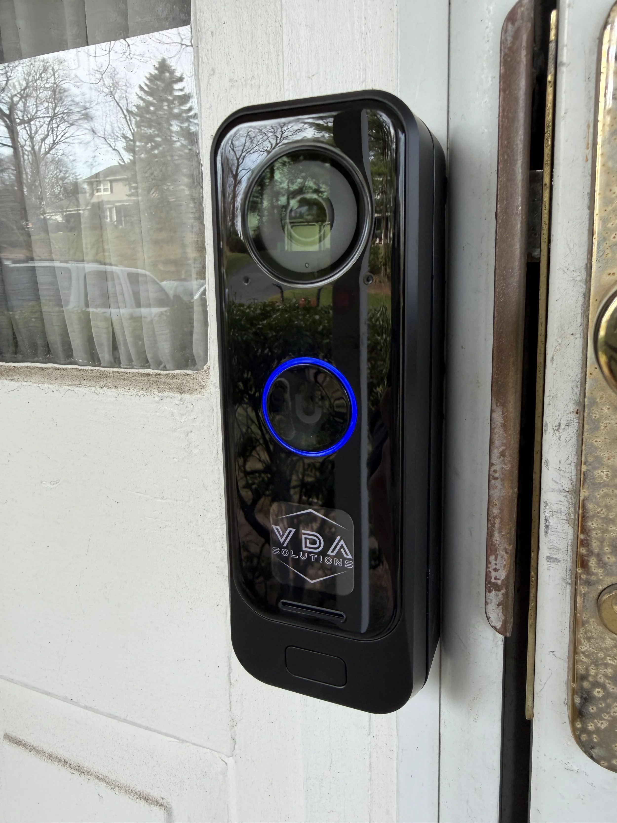 Digital doorbell with a camera and blue ring light mounted outside a house next to the door latch.