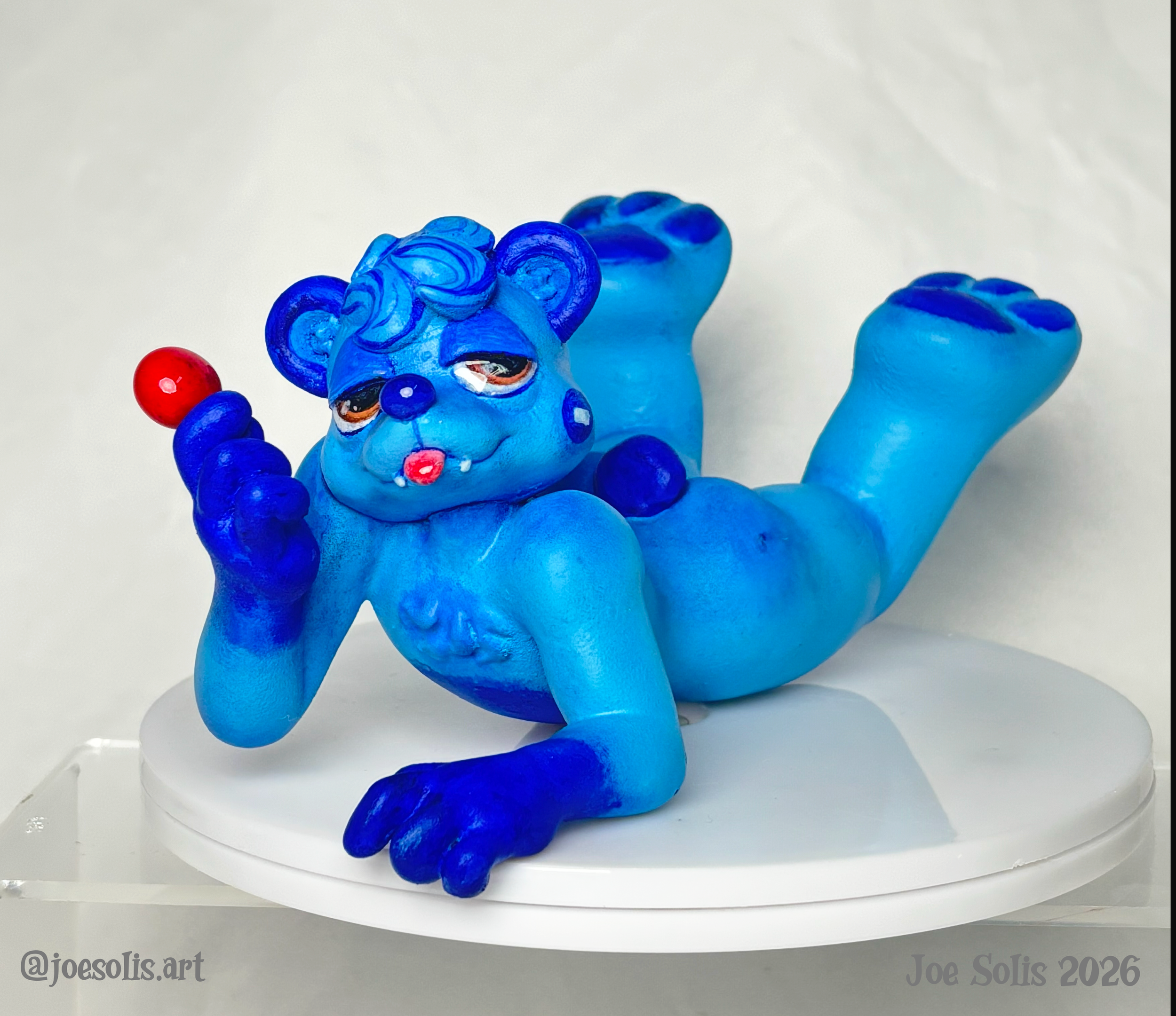 Blue sculpture of a lying animal with red and purple dots on its body, displayed on a white surface.