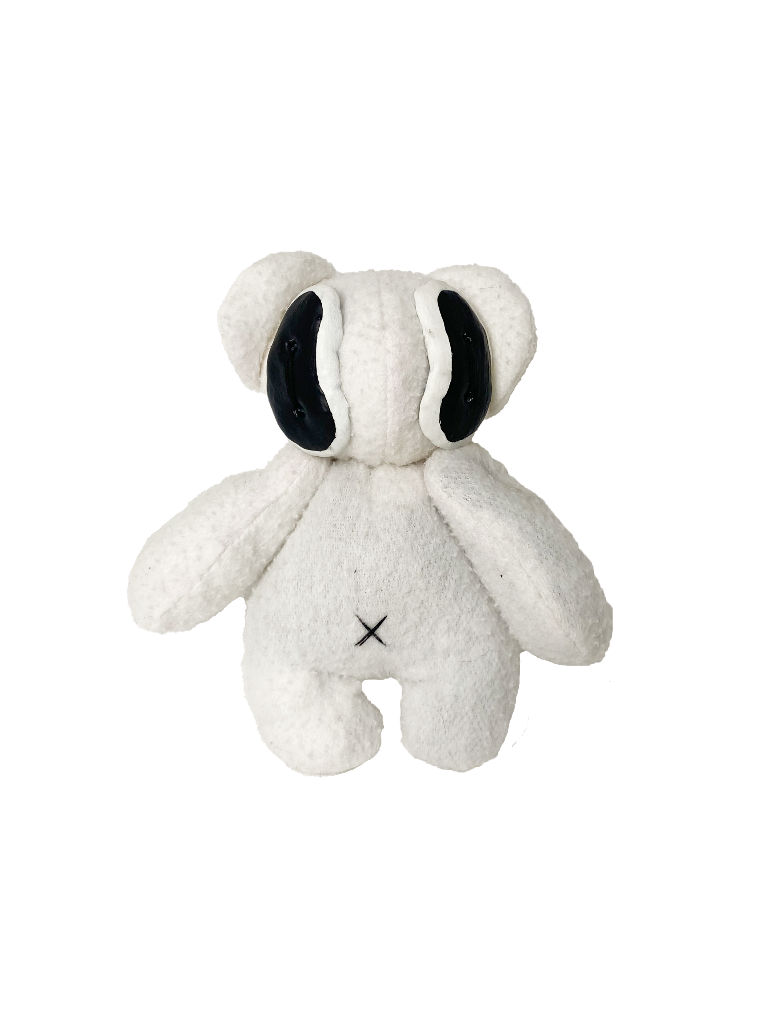 A white stuffed animal resembling a koala bear with black eye patches and a small black 'X' on its chest, sitting against a black background.