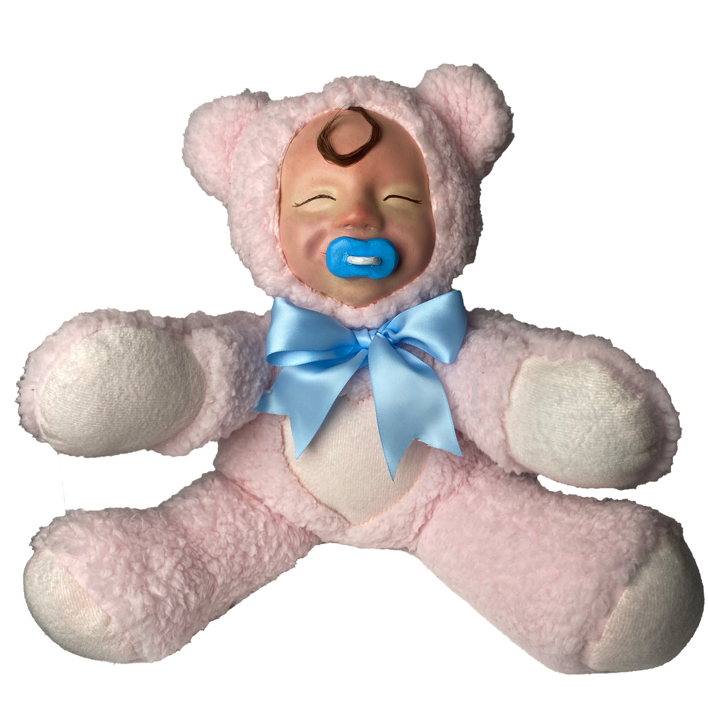 A baby plush with a pacifier in its mouth, wearing a fluffy pink bear costume with large round ears and a light blue bow around the neck.