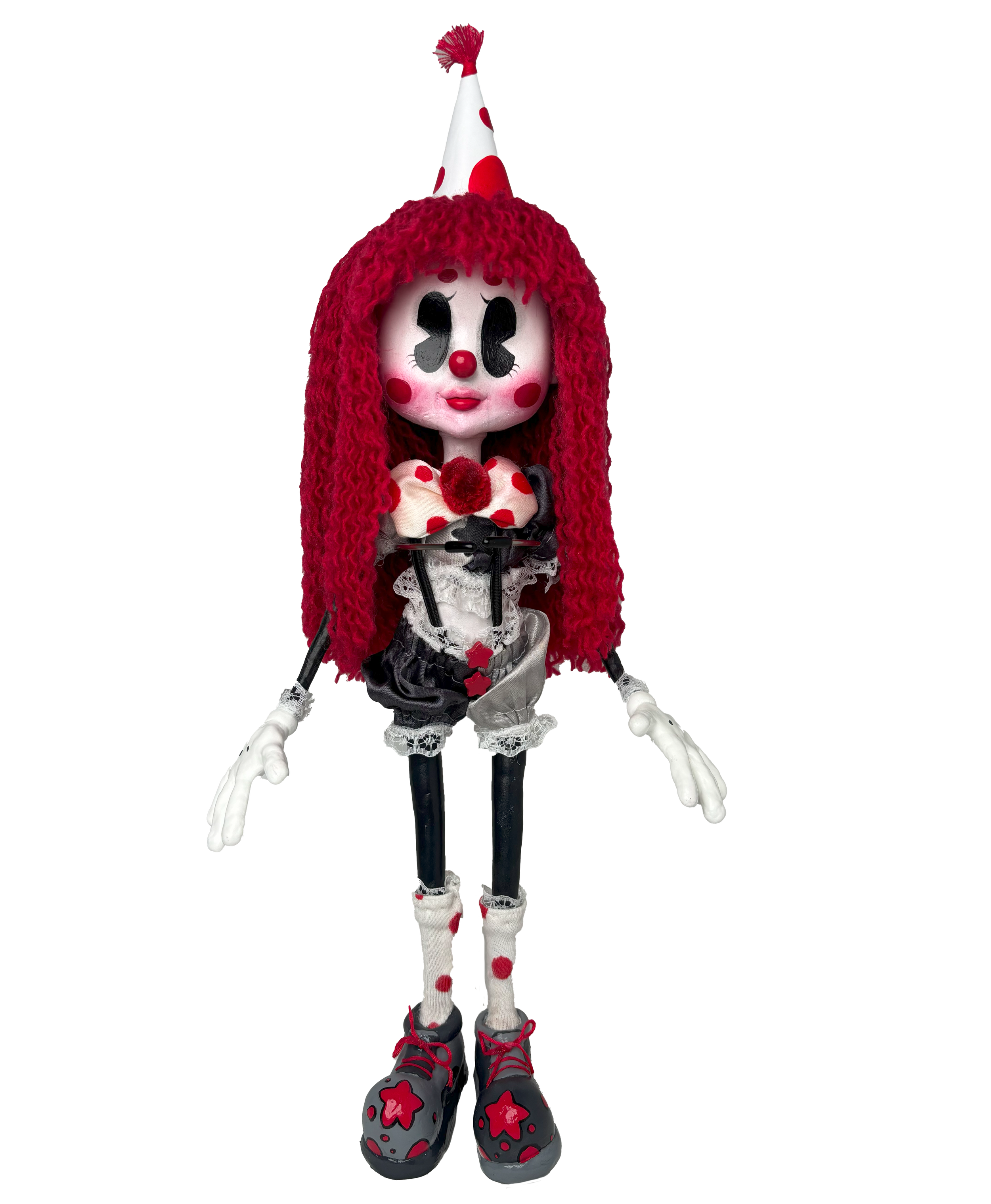 A doll dressed in a clown costume with a white face, red cheeks, and a red nose, wearing a red and white polka dot hat, red curly hair, and black shoes with red and pink flower designs, standing against a striped background.