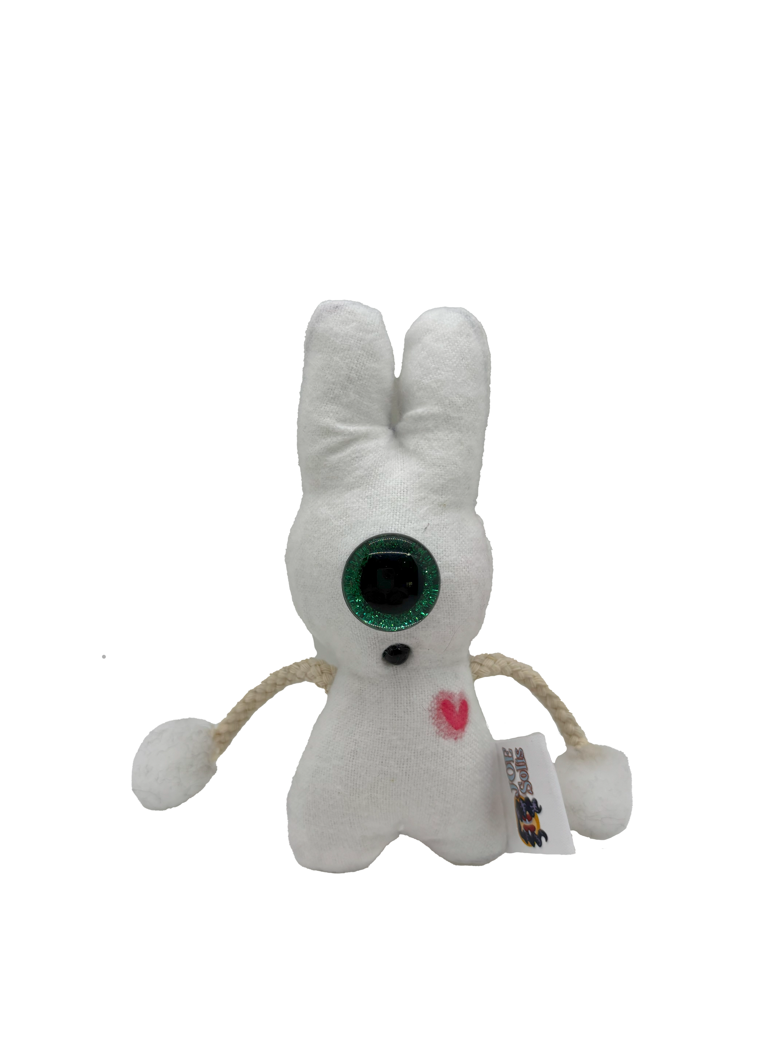 A small plush toy resembling a white bunny with a heart on its chest, large green eyes, a black nose, and wire-like arms and legs, standing upright.