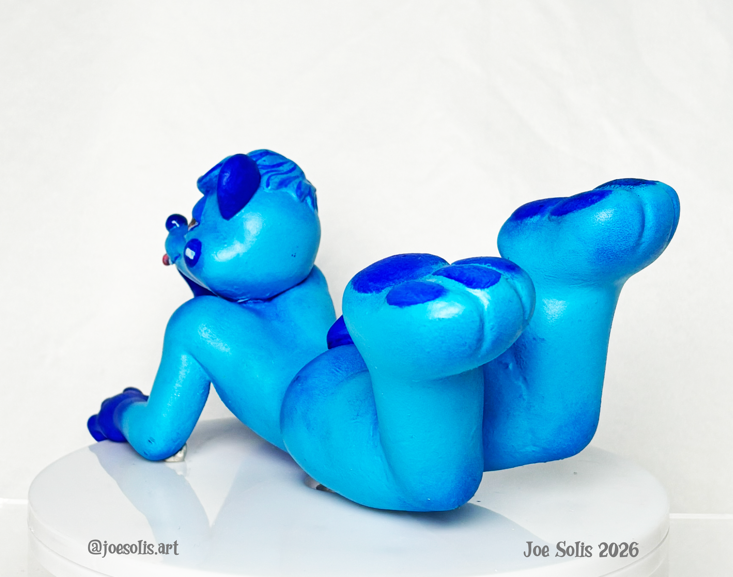 A sculpture of a blue octopus with a playful expression, positioned on a white round base, against a plain white background.