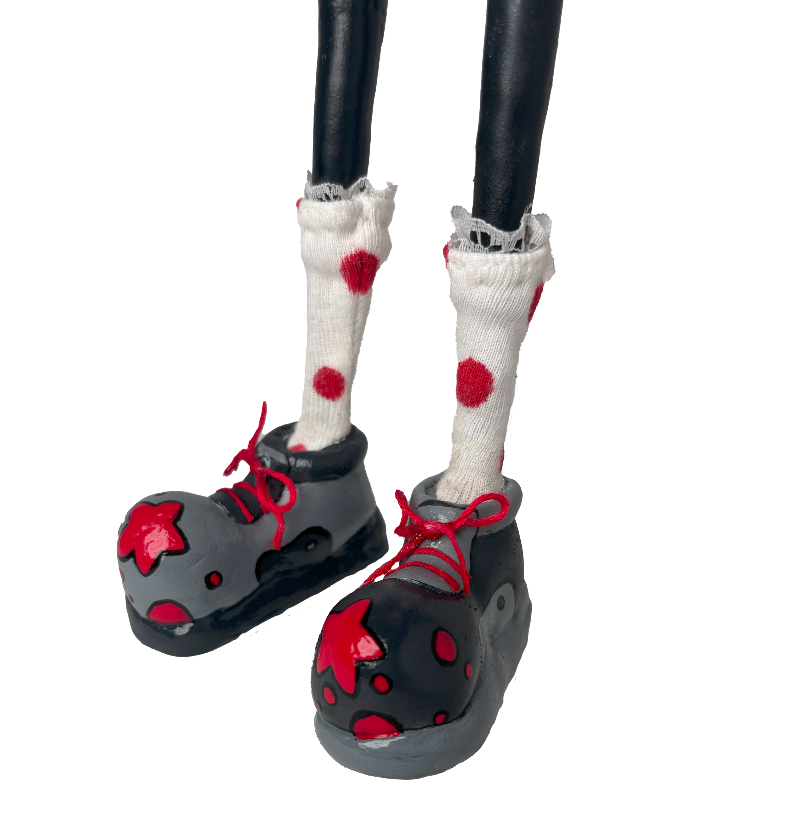 Close-up of a pair of black and red clown shoes with black laces, worn with white socks featuring red polka dots and frayed tops.