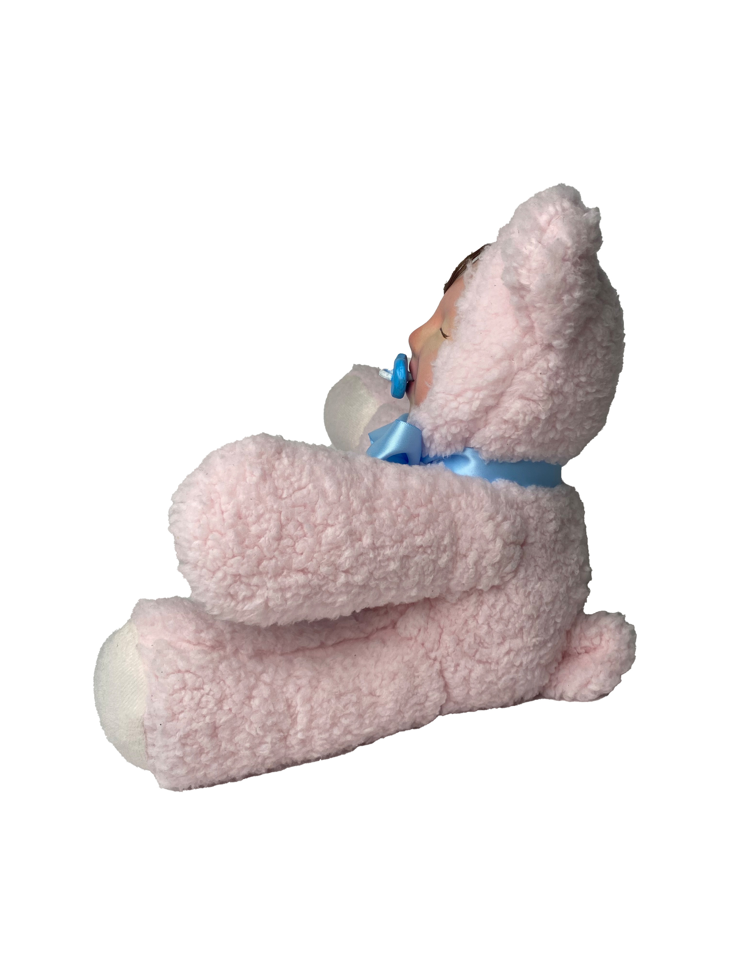 A baby wearing a pink fuzzy hat and matching pink fuzzy clothing, with a blue pacifier in their mouth, is sleeping.