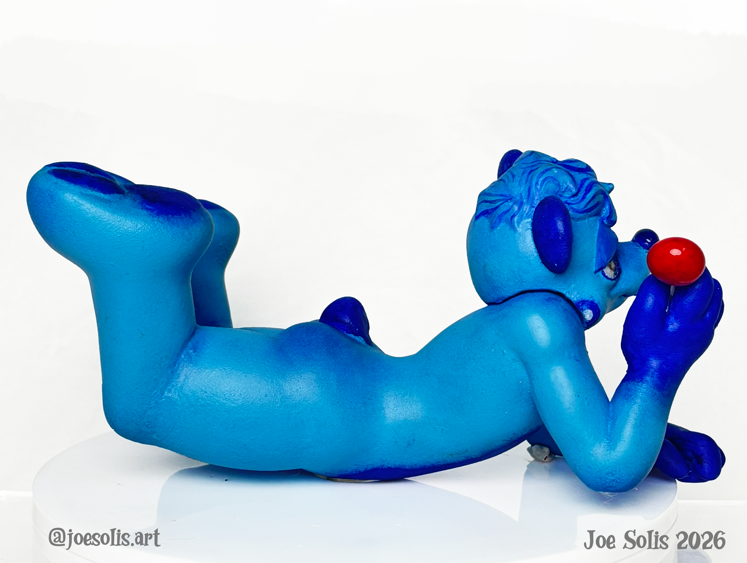 Blue sculpture of a mythical creature with a lion's head, eagle's body, and a red ball in its mouth, set against a white background.