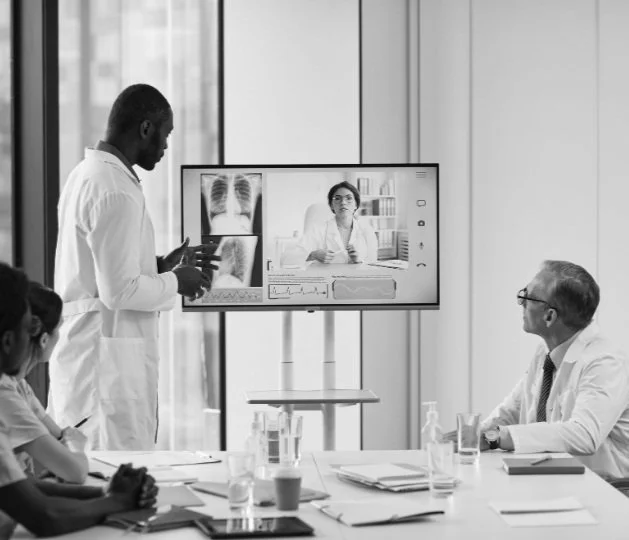 Medical team discussing X-ray images and a consultation via video conference in a modern hospital conference room.