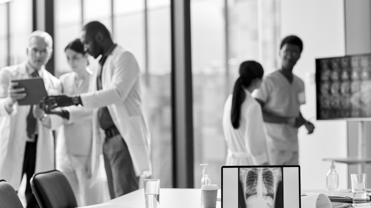 Doctors in discussion in a modern medical office with X-ray images of lungs on a computer monitor in the foreground.