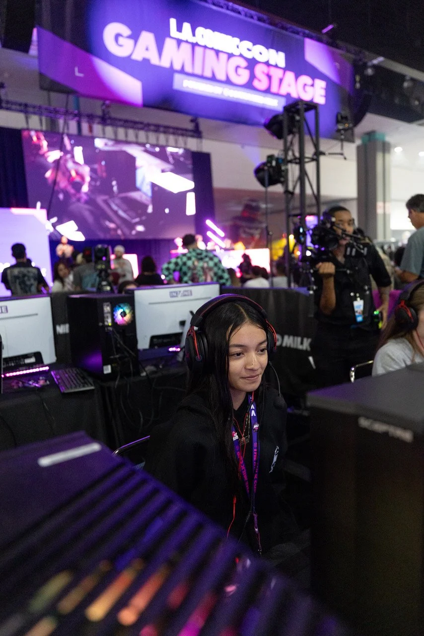 Large gaming event with people playing on computers in a crowded room, featuring colorful monitors and gaming equipment.