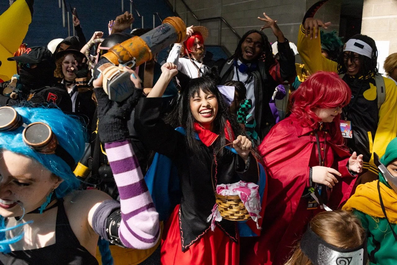 Person cosplaying as a character with a straw hat, red vest, and glasses, posing with fists up at a convention.
