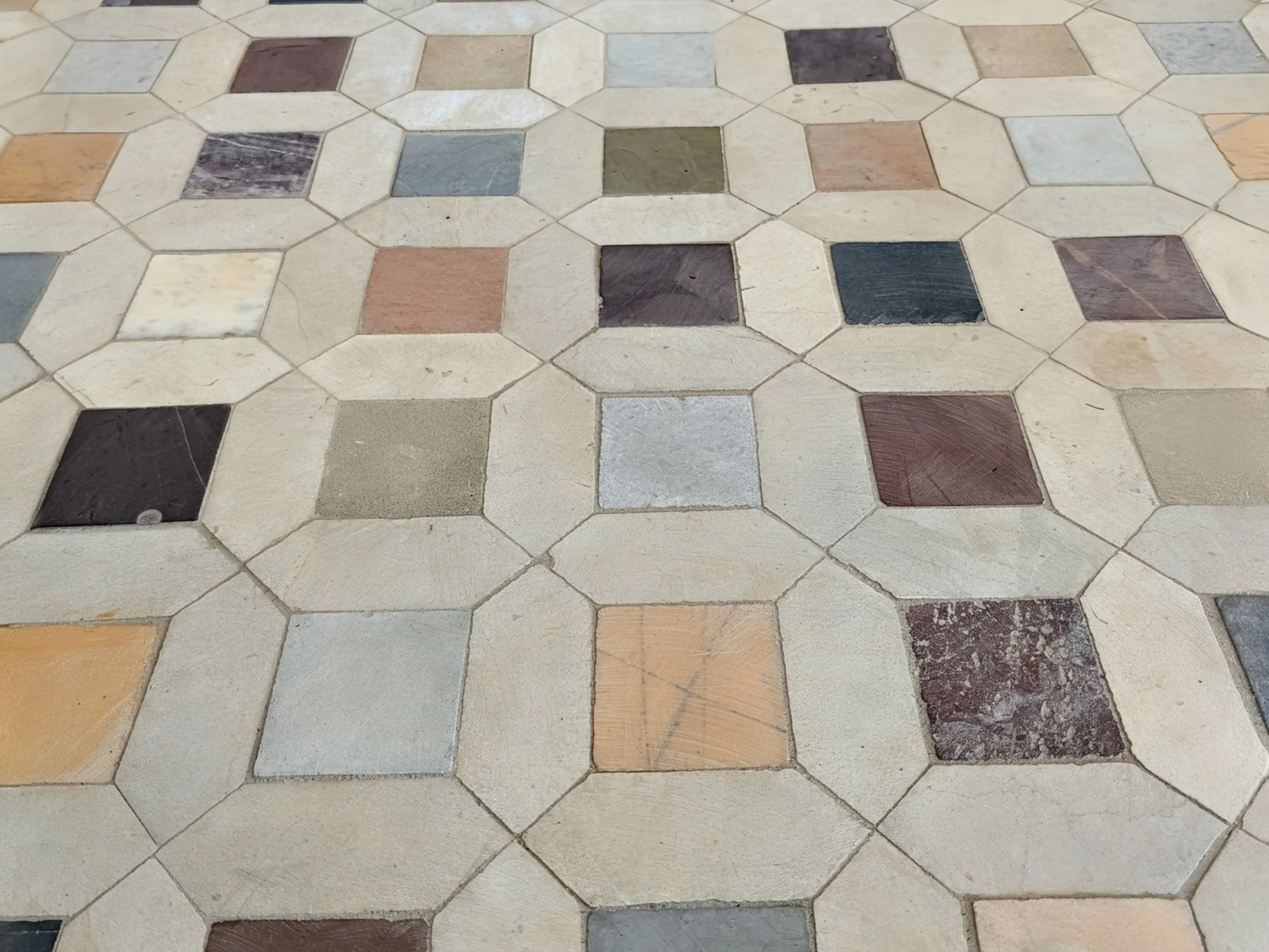 A tiled floor with honeycomb-shaped beige tiles and square tiles in various colors including black, gray, brown, and peach.