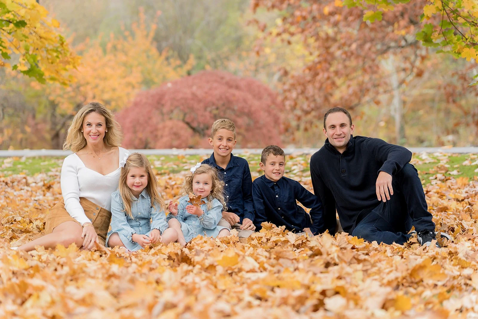 family sitting on top of leaves at a park smiling during fall photoshoot.
