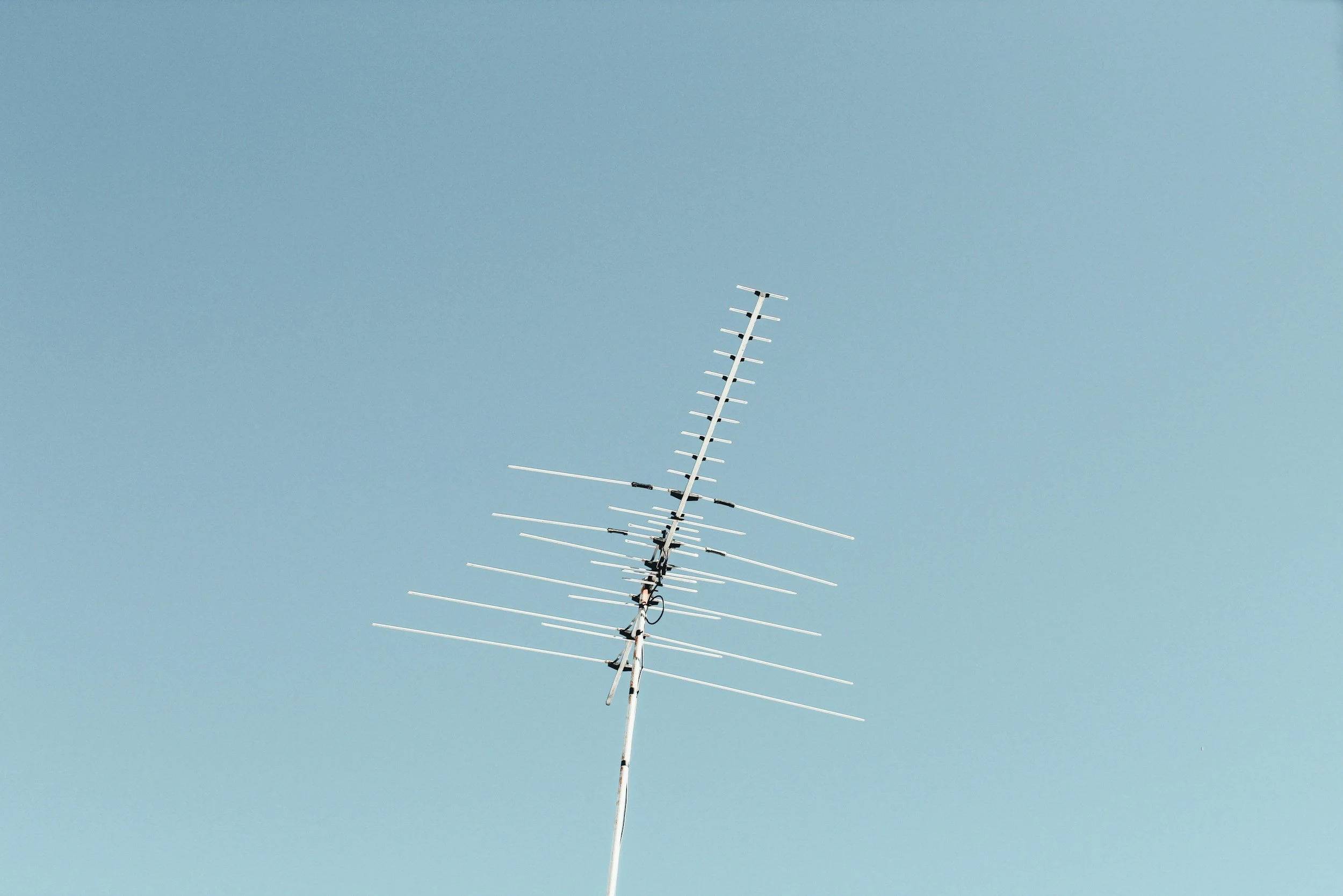 Television antenna mounted on a roof against a blue sky.