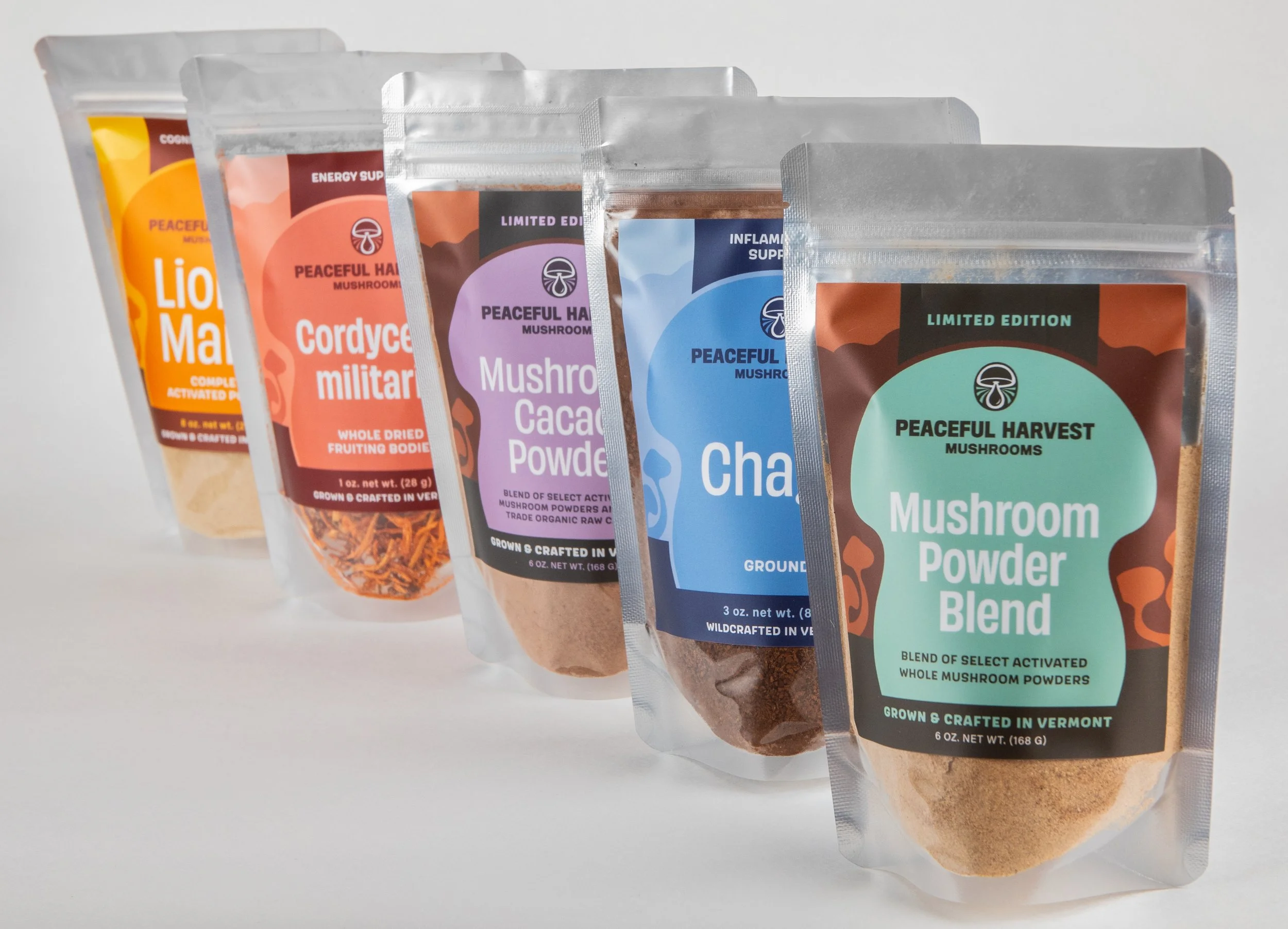 A row of five standing resealable pouches of mushroom powder blends and dried mushroom snacks with colorful labels, including flavors such as Lion Man, Cordyceps military, Mushroom Cacao Powder, Chaga, and Mushroom Harvest, on a plain white background.