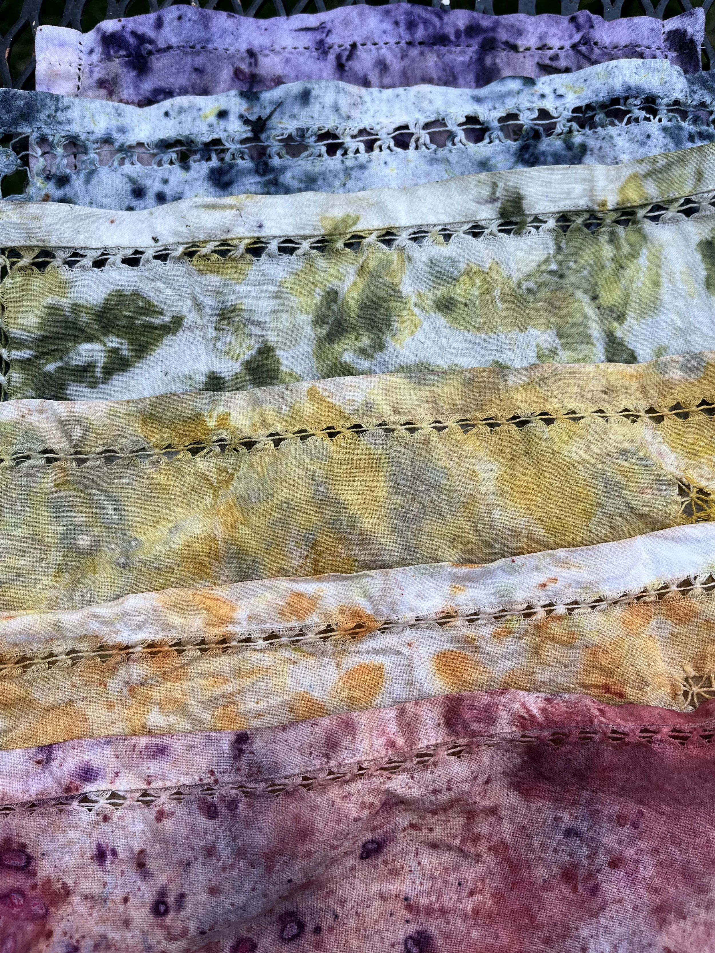 Multiple colorful fabric pieces with tie-dye patterns and decorative edges, arranged in horizontal layers.