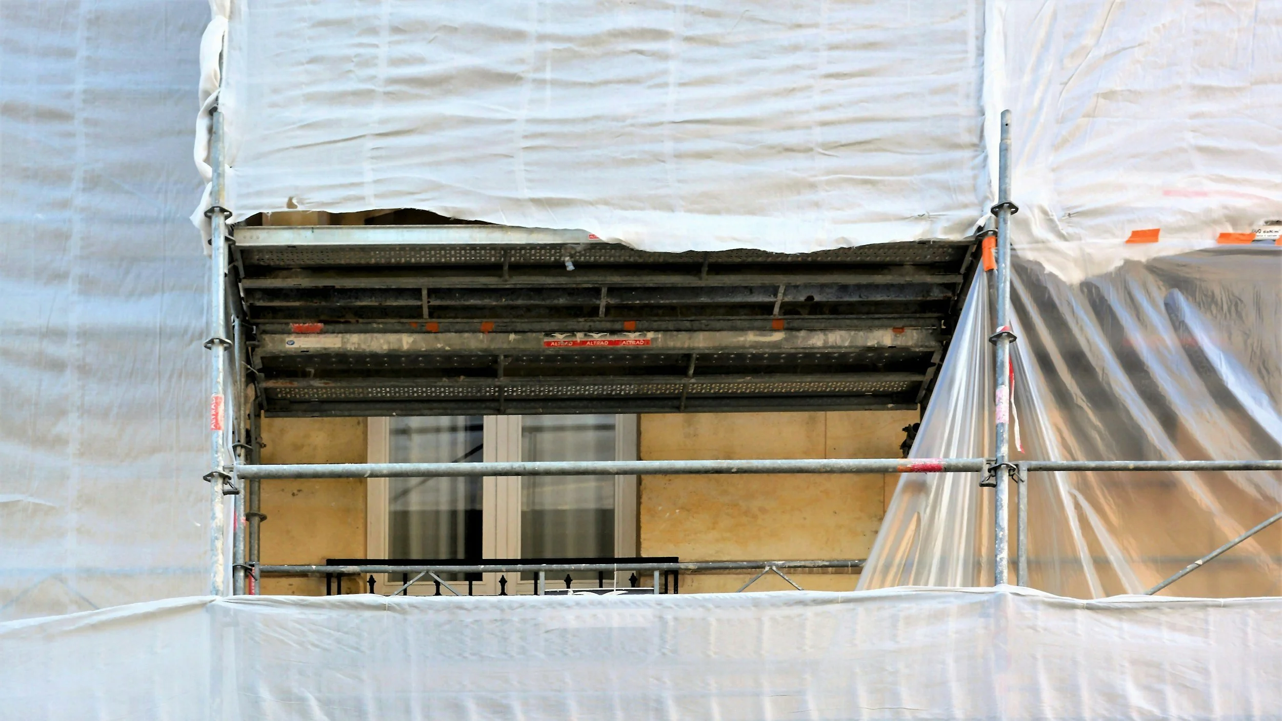 Vista de una fachada de edificio en construcción o renovación, rodeada de andamios y cubiertas plásticas blancas