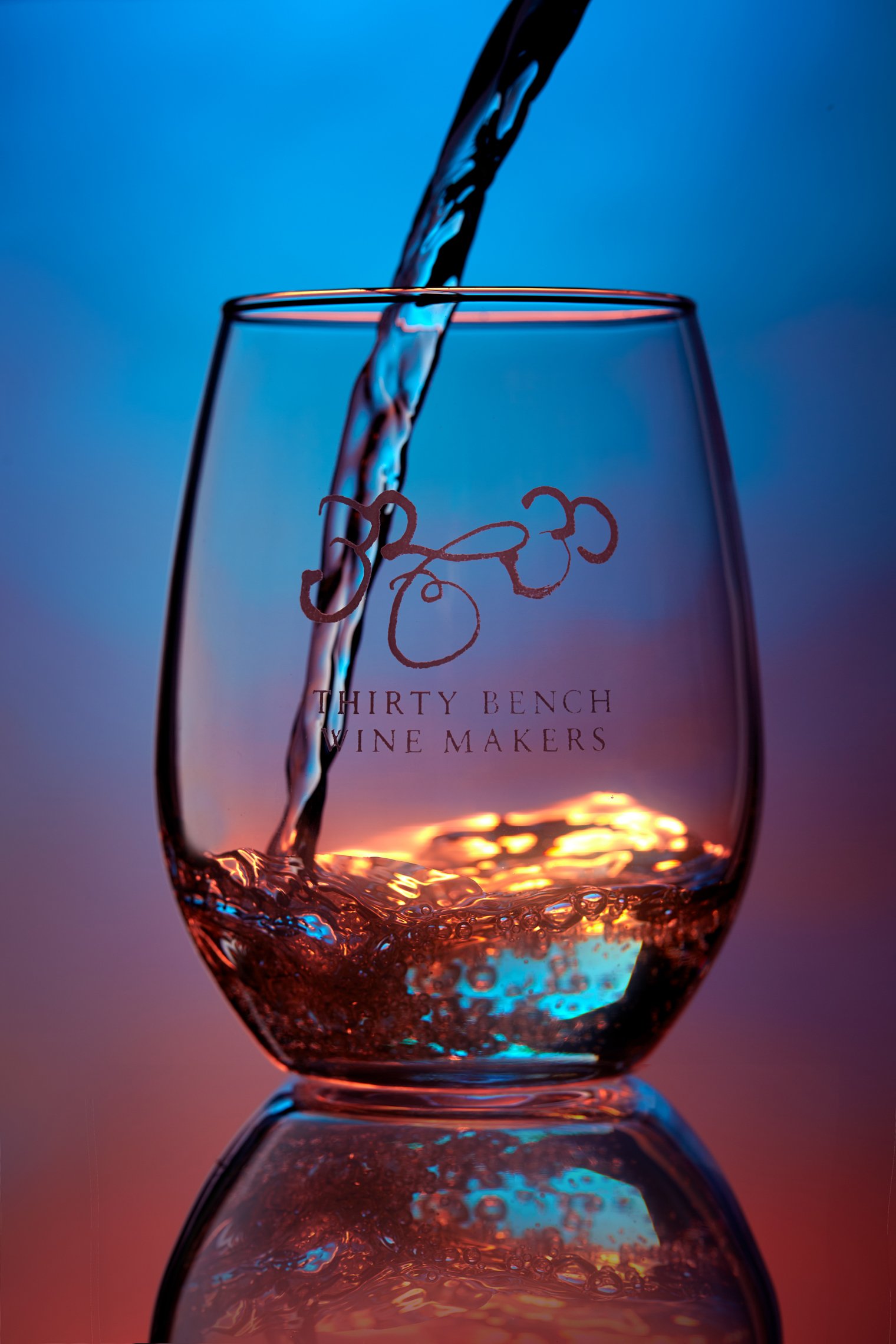 A glass of wine being filled with red wine, with colorful lighting and a logo that reads 'Thirty Bench Wine Makers'.