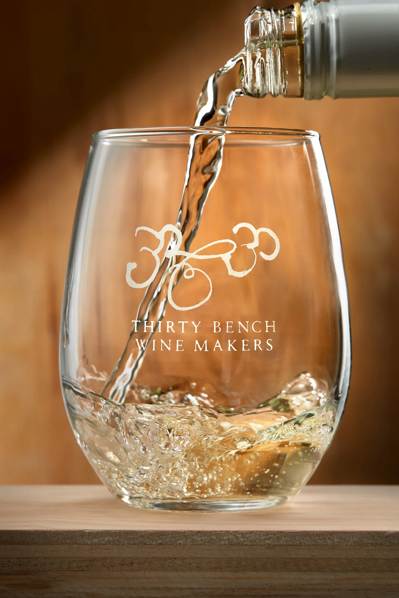 A glass being filled with white wine from a bottle, displaying the logo of Thirty Bench Wine Makers.
