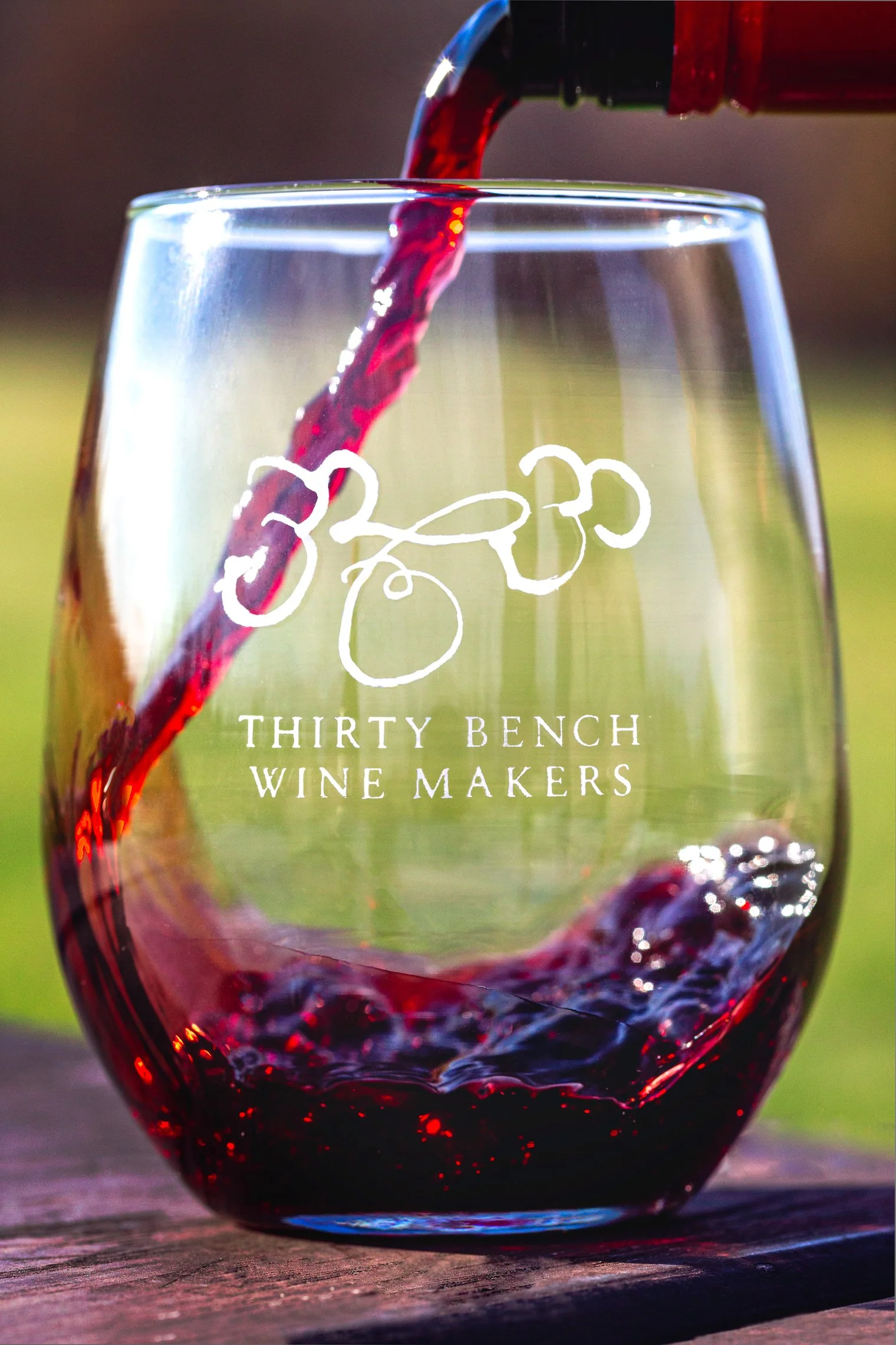A glass of red wine being poured from a bottle, with a logo and text that reads 'Thirty Bench Wine Makers' on the glass.