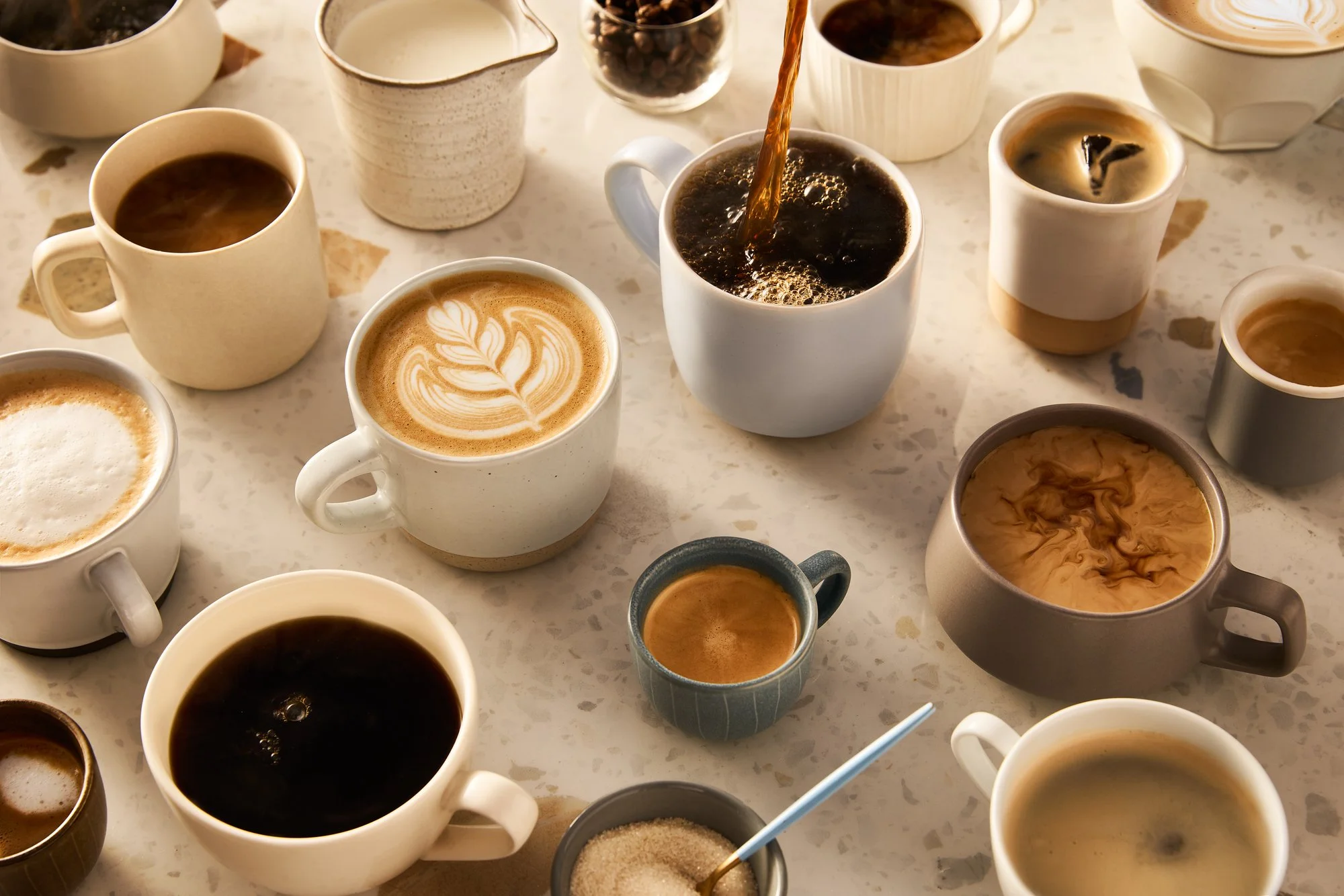 Various cups of coffee and espresso on a table, including a latte with latte art, black coffee, and coffee with cream, in different cups and mugs.