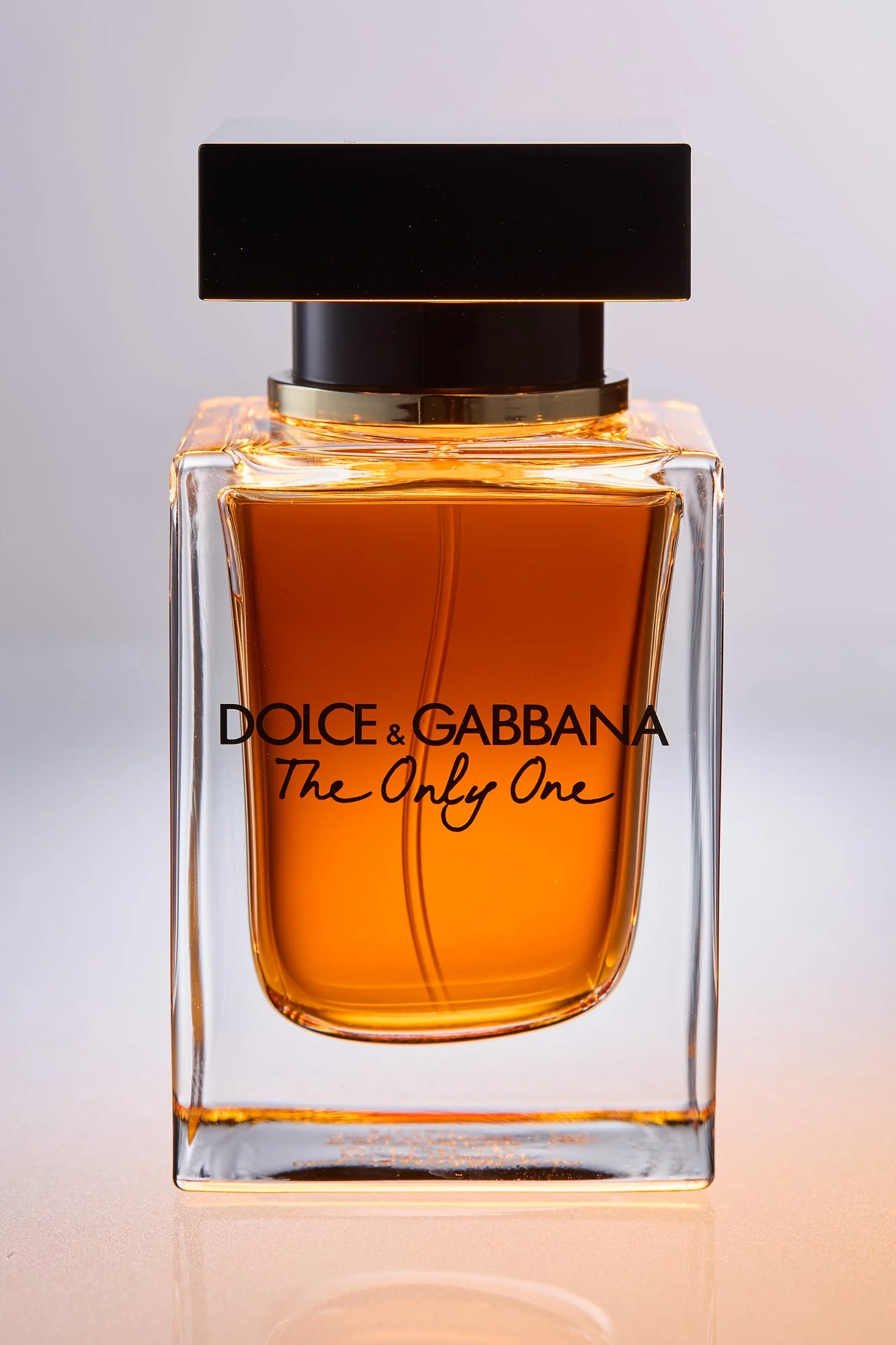 A close-up of a Dolce & Gabbana perfume bottle labeled "The Only One" with a black cap and amber-colored perfume inside.