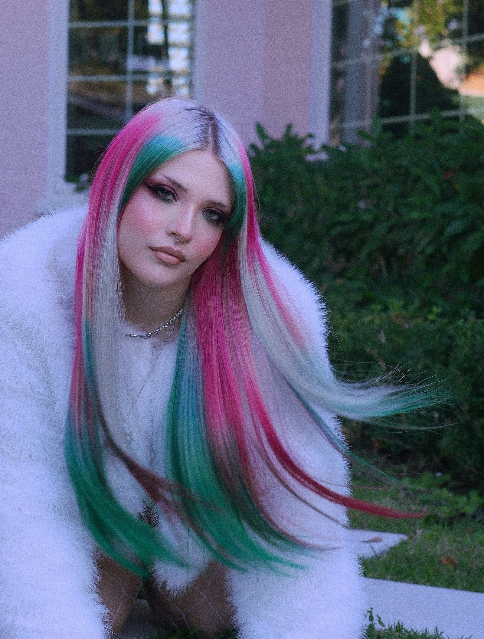 Young woman with long, multi-colored hair in pink, green, and blue shades. Tape-in hair extensions. Vivid and platinum hair extensions styled in a long disconnected mullet.