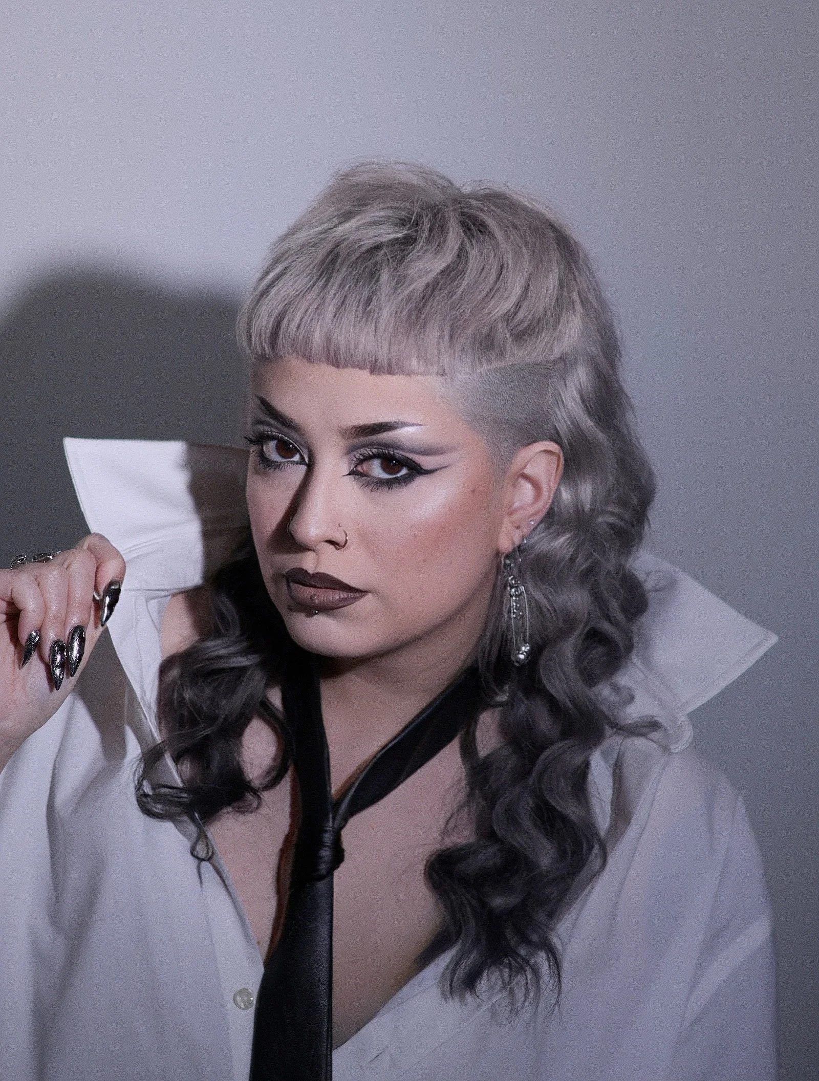 A woman with platinum blonde hair styled in an undercut mullet. Platinum grey reverse ombre. Punk hair. Alternative hair. 