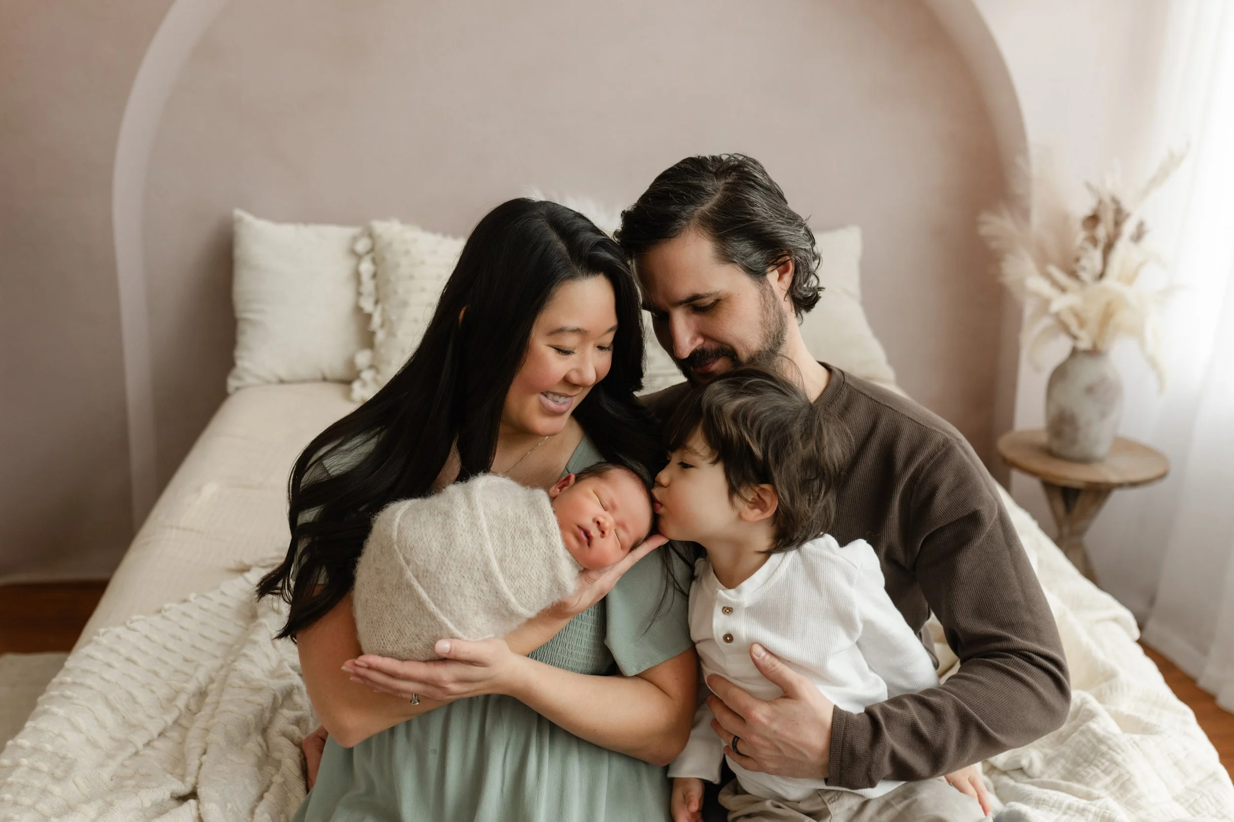 snuggly family photo on bed with brother kissing baby, trussville birmingham alabama