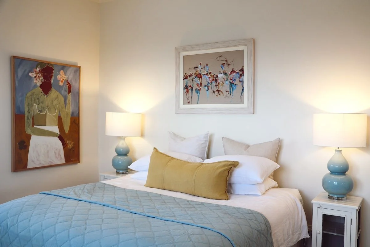 A bedroom with a bed, two bedside lamps, and three paintings on the wall