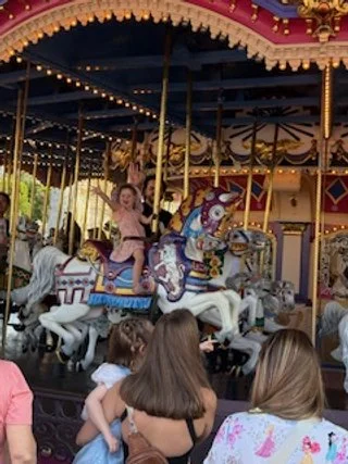 Child riding a carousel horse at an amusement park, with spectators watching.