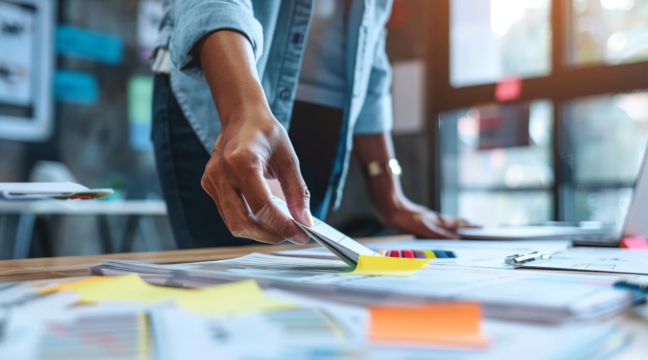Someone organizing papers and sticky notes on a desk in an office