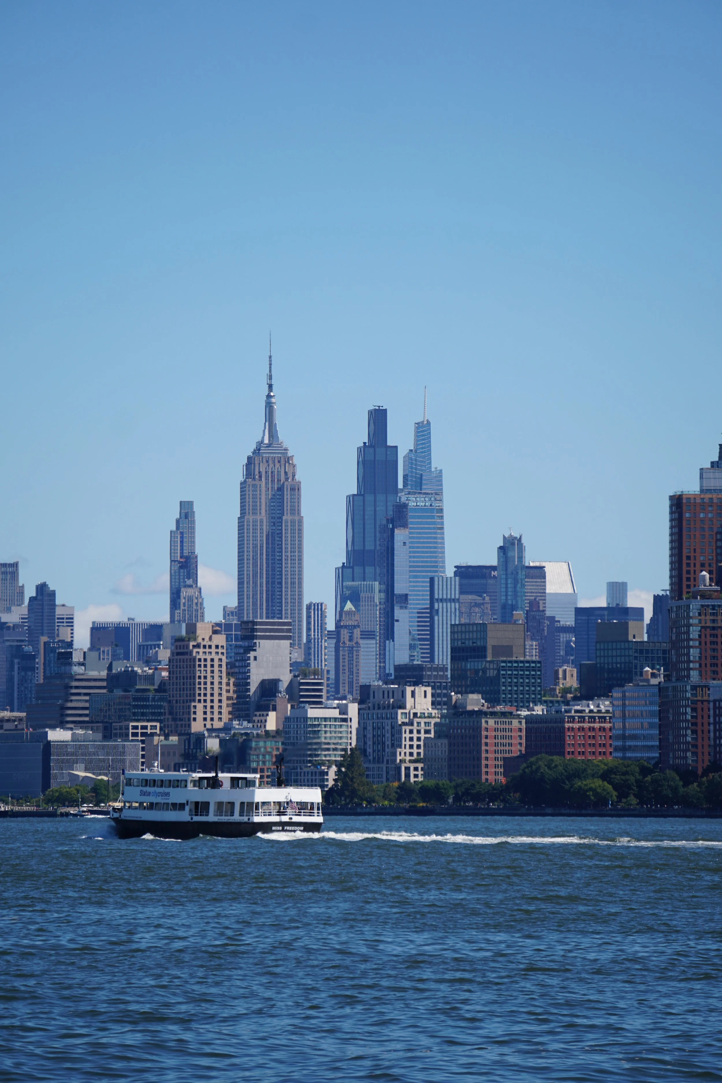 A boat on water with a city skyline featuring tall skyscrapers, including the Empire State Building, in the background.
