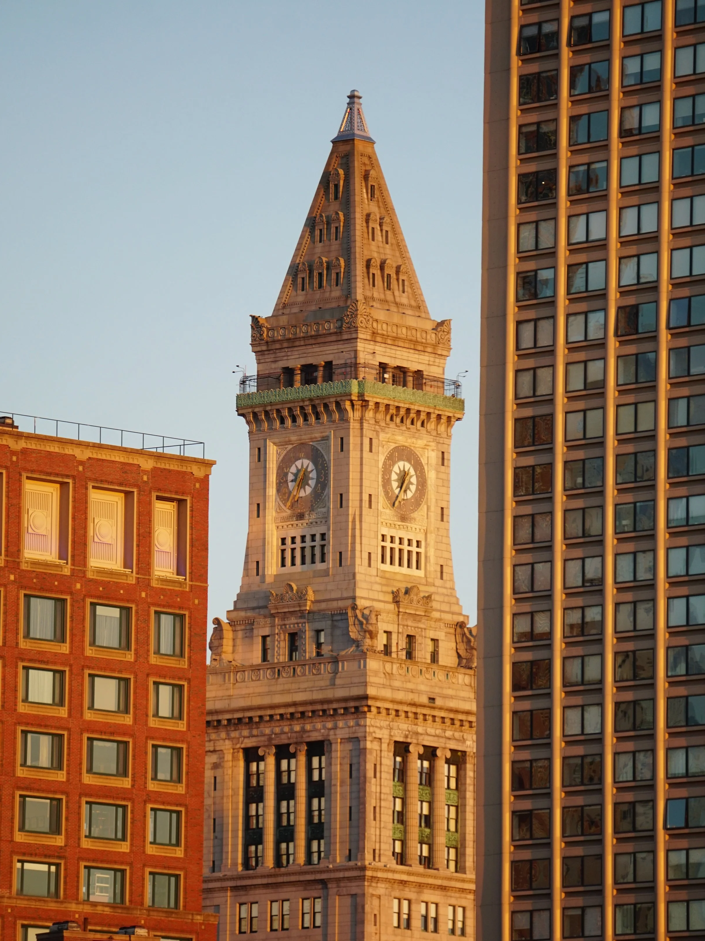 Close-up of the historic Boston Tower with a clock, surrounded by modern and historic buildings in downtown Boston, during sunrise.
