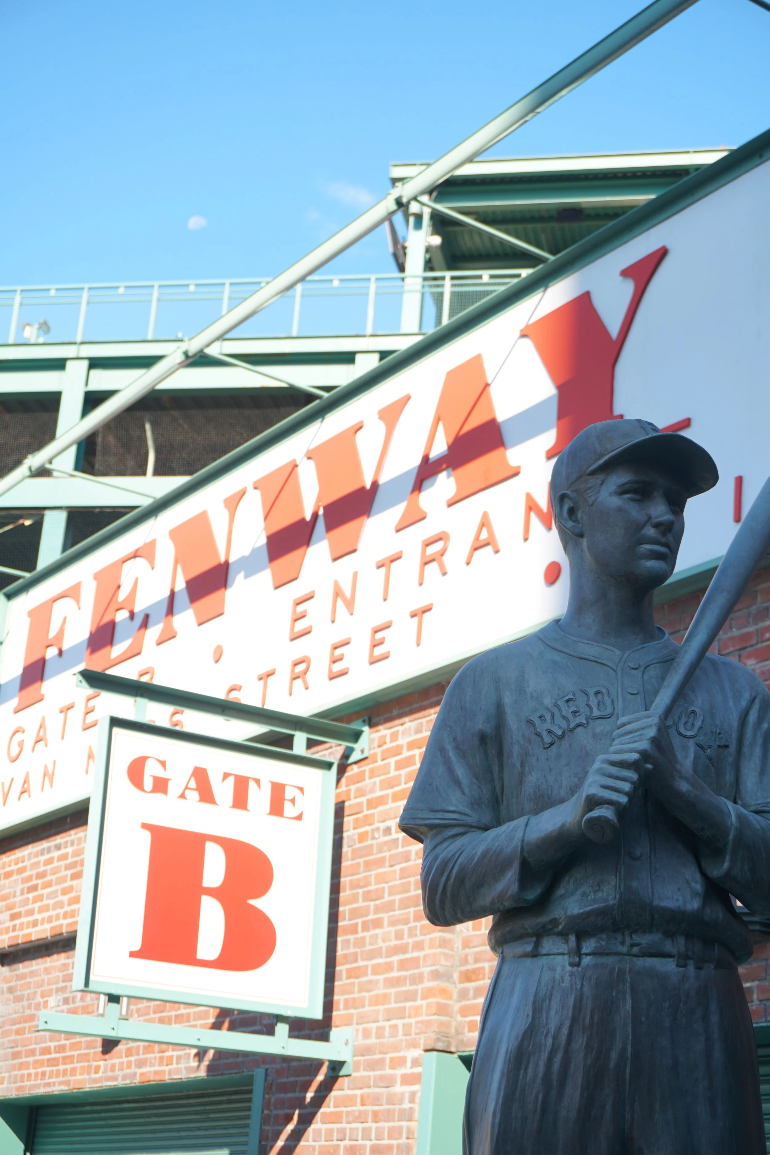 Statue of a baseball player holding a bat in front of Fenway Park signage, including Gate B, in Boston, Massachusetts.