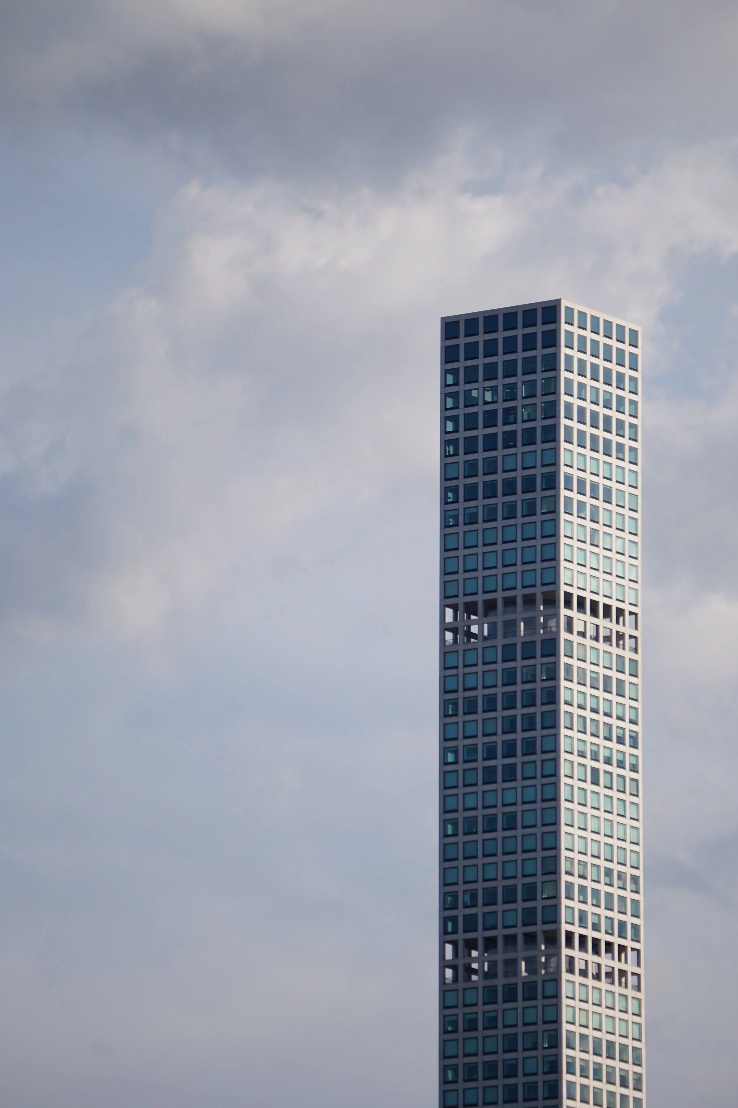 A tall modern skyscraper with a grid-like pattern of windows against a partly cloudy sky.