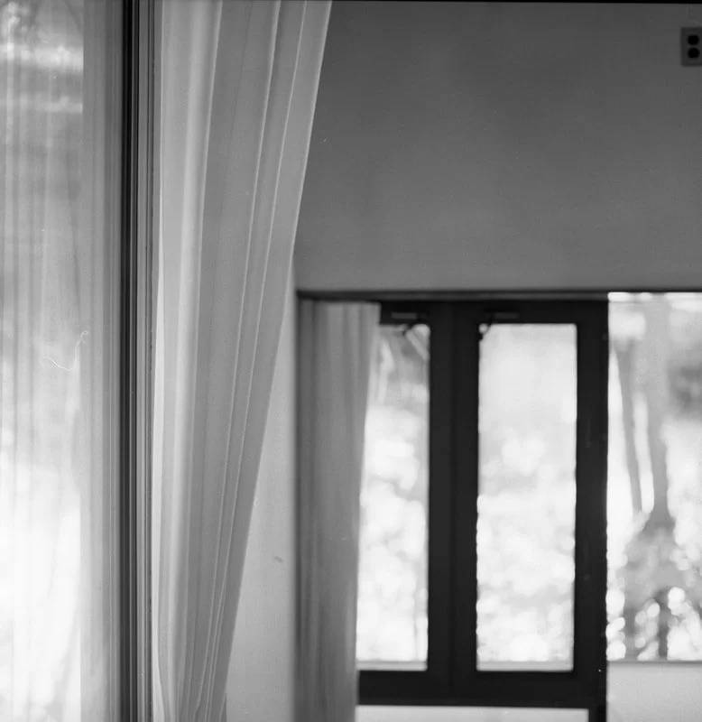 Interior view of a room with curtains and large windows showing trees outside.