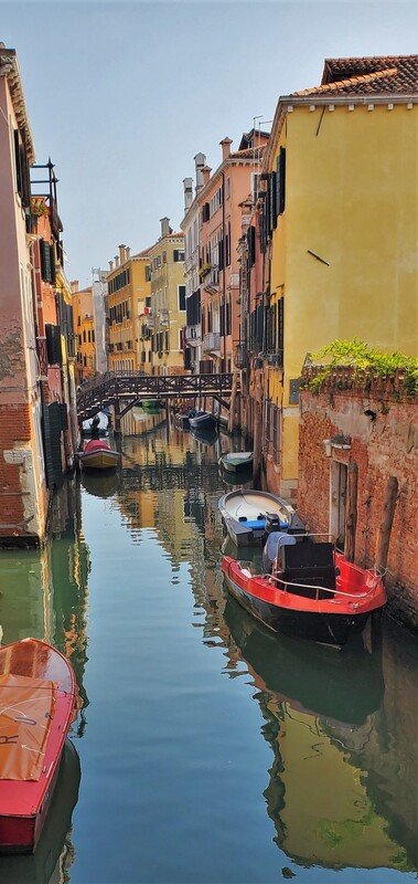 Colorful buildings line a narrow canal with boats docked along the sides in Venice, Italy.