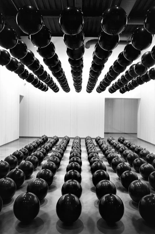 A room filled with black exercise balls arranged in rows, with additional balls suspended from the ceiling in a grid pattern.