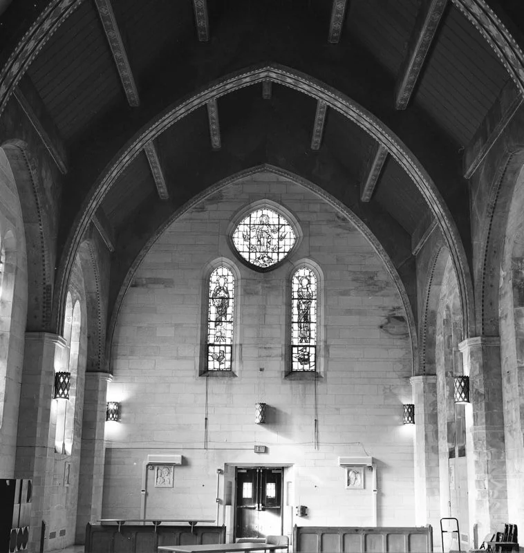 Interior of a church with high arched ceiling, stained glass windows, and wooden benches.