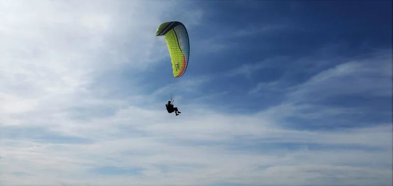 Person hanging from a blue and yellow kite flying in the sky.