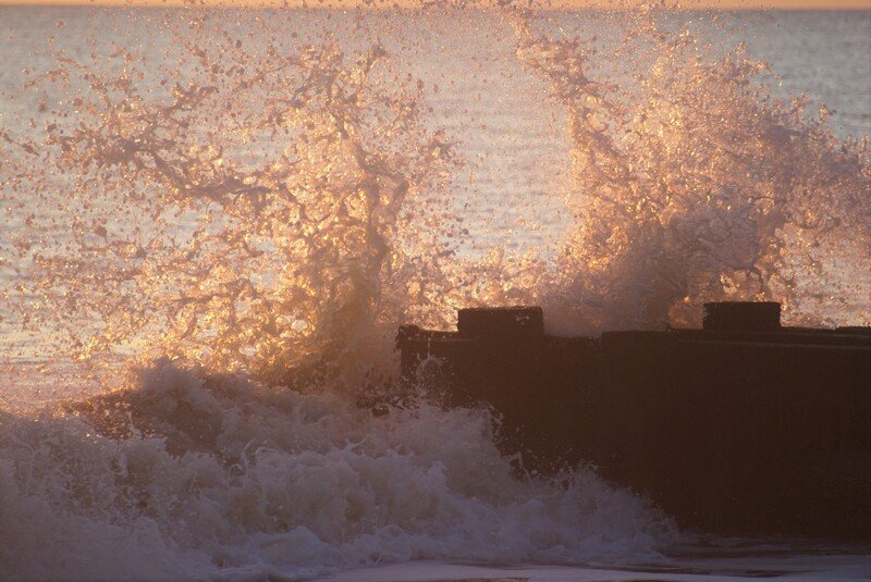 Waves crashing against a pier or seawall during sunset or sunrise.