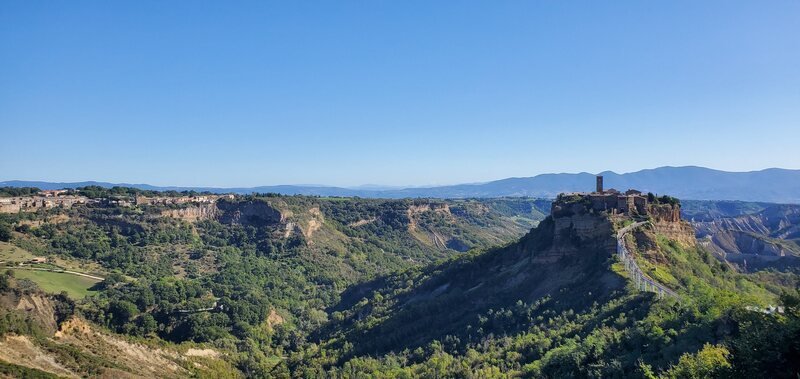 View of a canyon with a castle on a hilltop, surrounded by green vegetation and distant mountains under a clear blue sky.