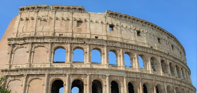 Close-up of the Roman Colosseum with arches and columns against a clear blue sky.