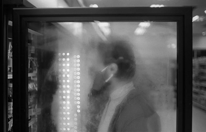 A person wearing a face mask looking inside a refrigerator in a store aisle.