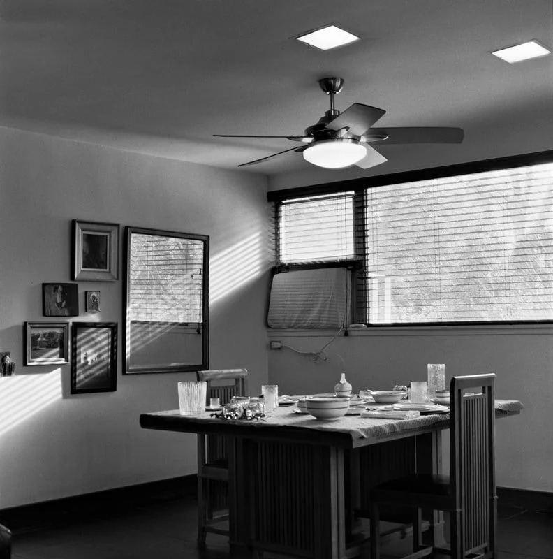 A dining room with a table set for a meal, illuminated by sunlight through a window.