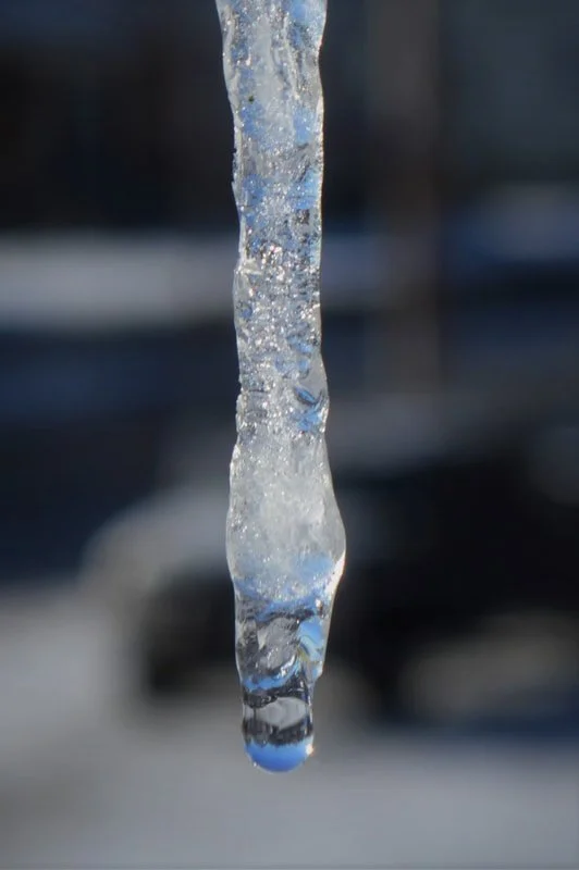 Close-up of an icicle hanging outdoors with blurred background.