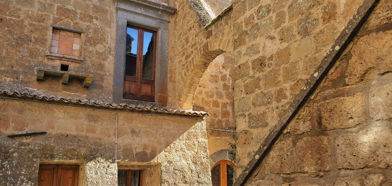 Close-up of an old brick and stone building facade with a wooden door, window, and an archway, in a rustic style.