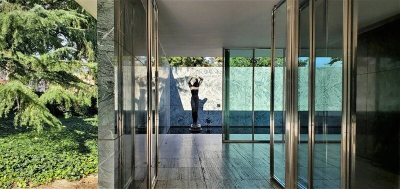 A person standing on a scale inside a modern building with glass sliding doors, with trees visible outside.
