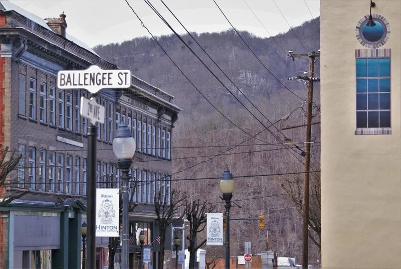 Street scene with buildings, street signs, and lamp posts on Ballengee Street, against a backdrop of leafless trees and hills.
